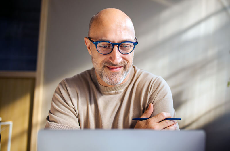 Professional businessman with glasses working on a laptop in a sunlit room, using Anthropic AI tools to enhance productivity.