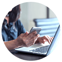 Businesswoman holding smart phone while working off of her notebook computer