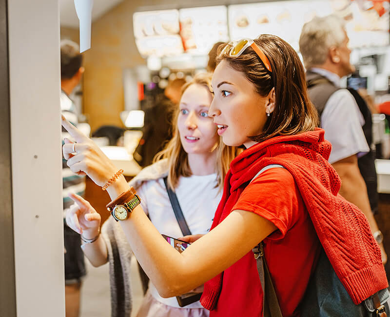 Customers using touch display kiosk in modern restaurant