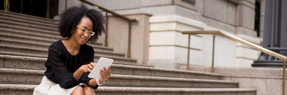 Business woman checking email on her personal tablet computer sitting on the steps of a government building