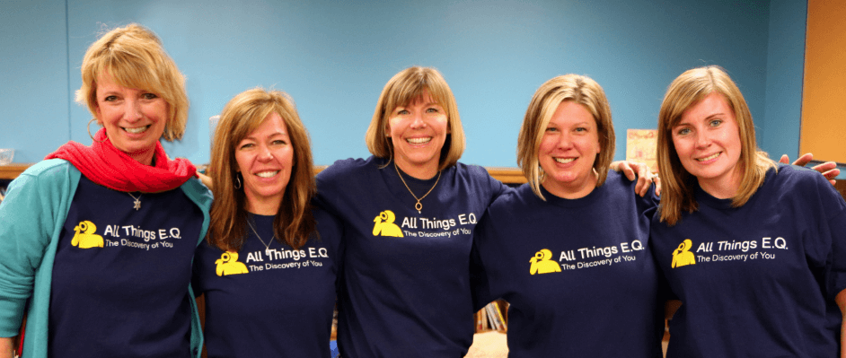 Five women stand together smiling. They are wearing AVA School Solutions T-shirts that say "All Things E.Q (Emotional Quotient) the Discovery of You".