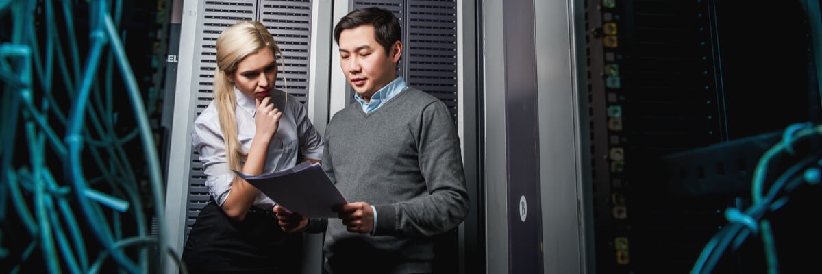 Woman and man standing in a server room, looking at files.