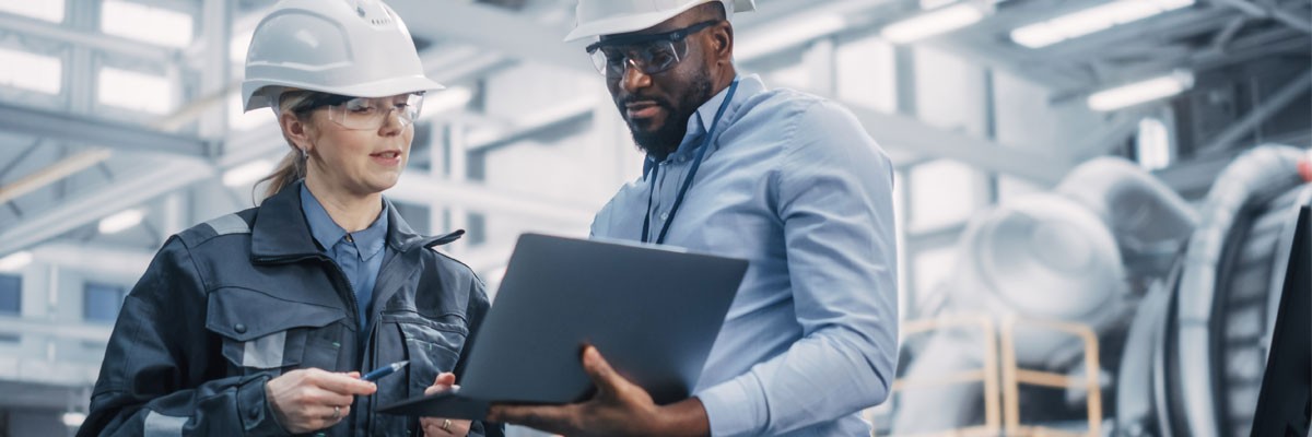 Two engineers on factory floor looking at laptop computer