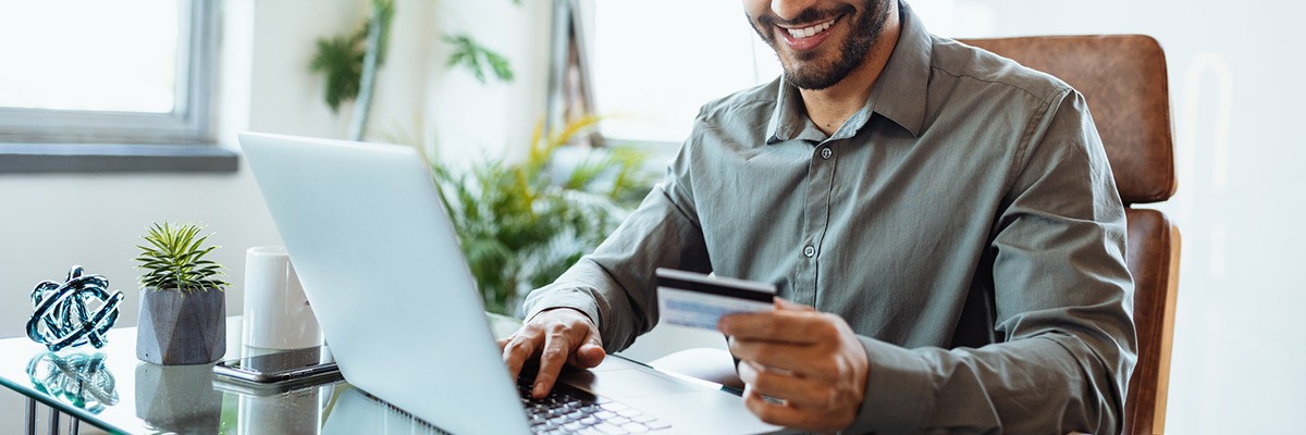 Man smiling working on laptop holding credit card