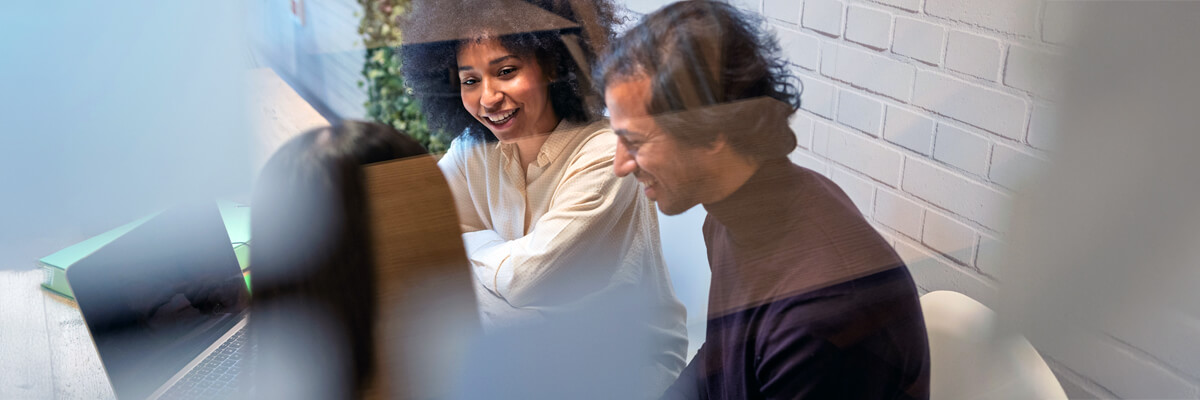 Three colleagues collaborate at a laptop in a modern workspace, discussing project details and refining work plans with AI.