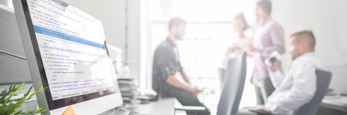 Close up of code displayed on computer screen with development team in the background