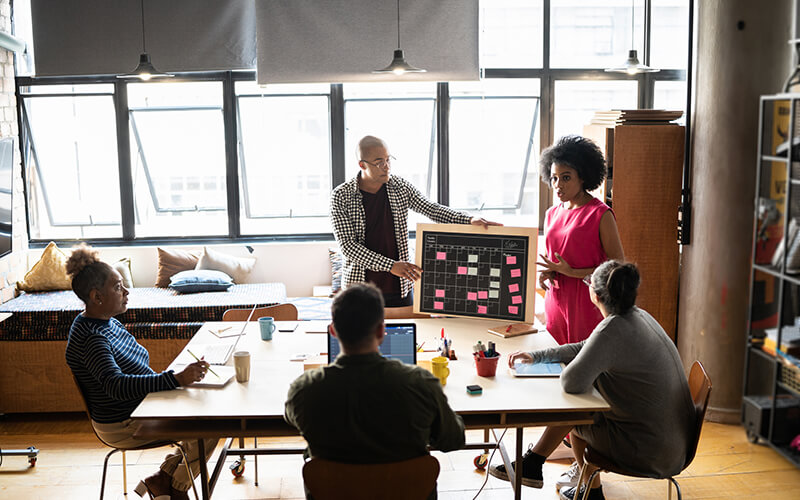 Collaborative team gathers around a table in a bright office to review a shared list of project activities.