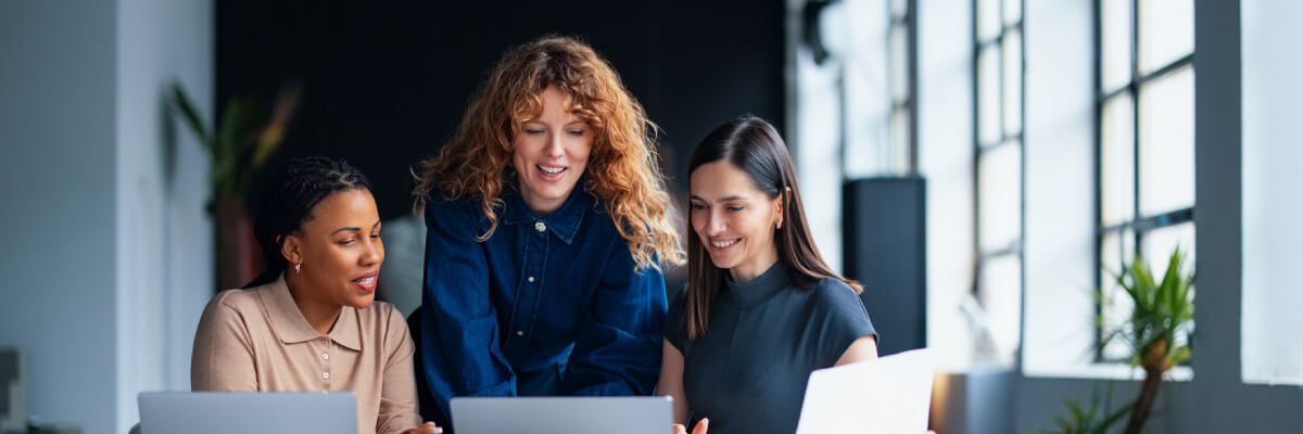Diverse professionals collaborate on a laptop using Google Workspace in a sunlit, modern open-plan office.