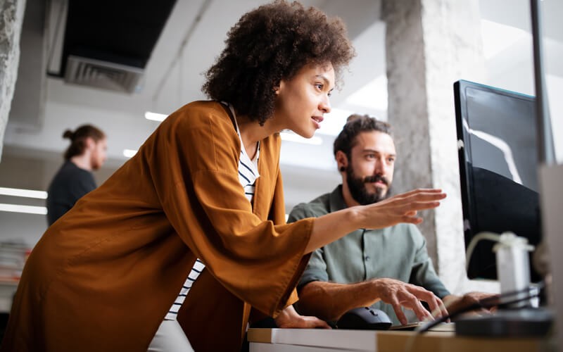Two colleagues reading case studies on desktop computer