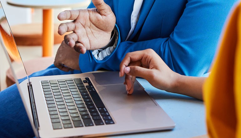 Two business colleagues collaborating in workplace over laptop computer