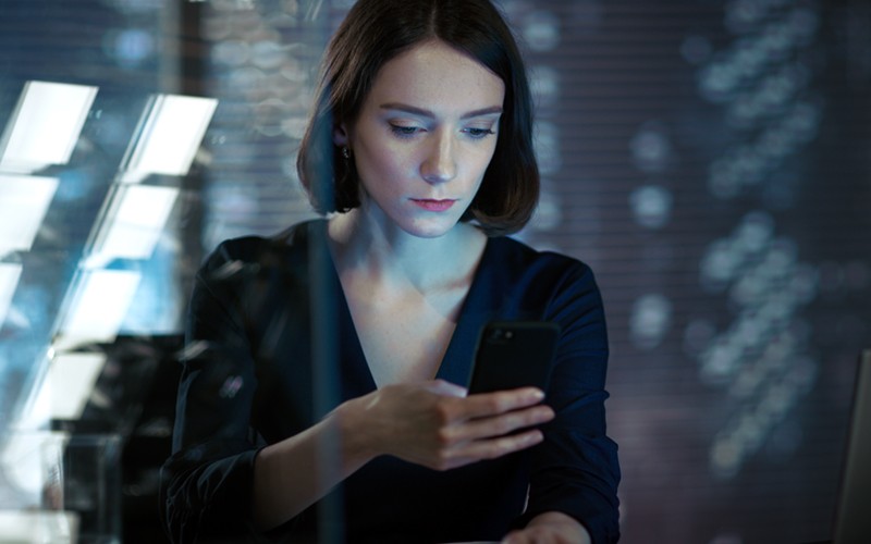 Bolster your organization’s defenses Businesswoman on mobile device in office at night