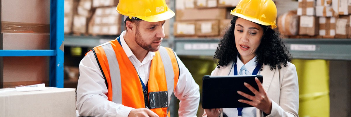 Two manufacturing employees in warehouse using tablet device