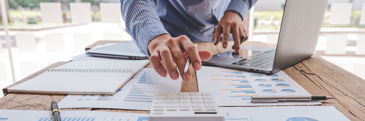 Financial analyst reviewing data with laptop computer while using calculator 