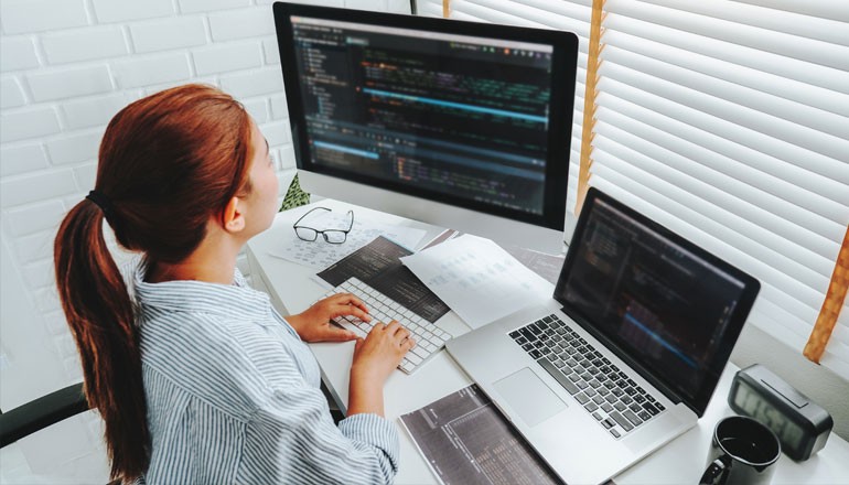 Make corrections and add new features to your software as needed Female developer works at desk with multiple monitors
