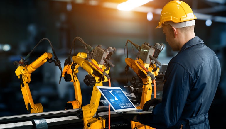 Worker in hard hat on laptop computer working in manufacturing facility 