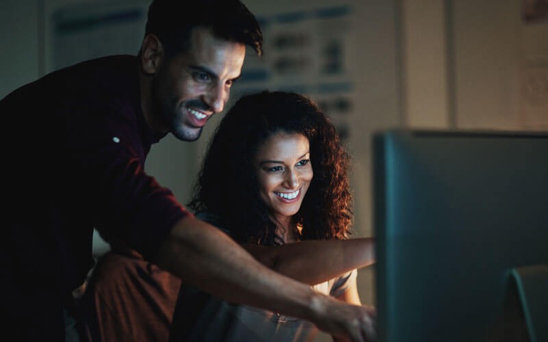 Two users collaborating in front of monitor smiling