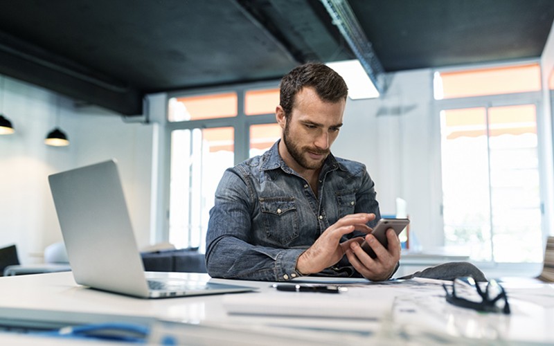 Business professional checking email on smart phone at his desk