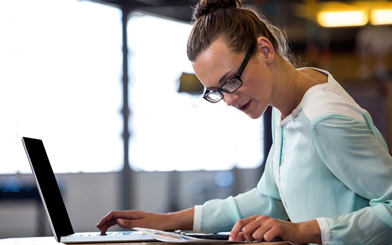 Female employee working on laptop and looking at document