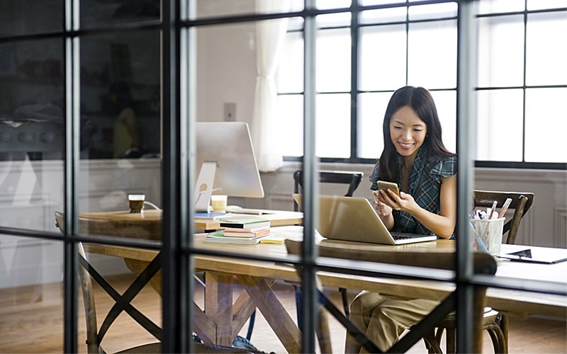 Business woman in office smiling at mobile device and laptop
