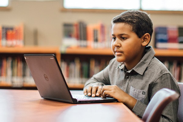 Student doing homework at desk in library on a Dell Chromebook netbook