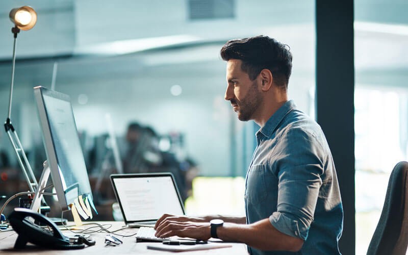 worker-focused-at-desk-using-laptop-and-monitor