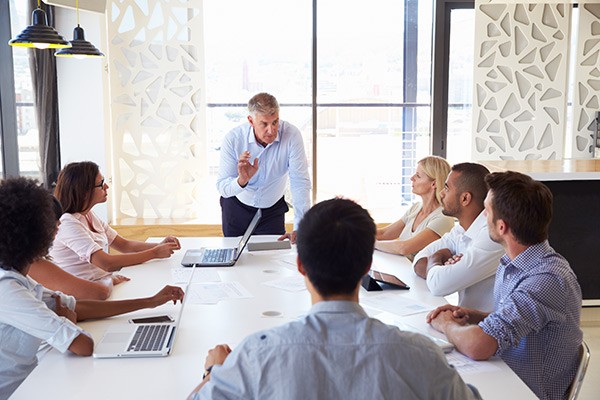 Businessman on laptop leads team meeting