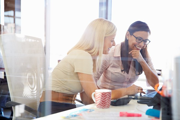 Women at a desk smile and discuss work 