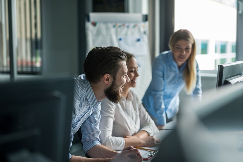 Young team of 3 office workers looking at monitor enthusiasticallly.