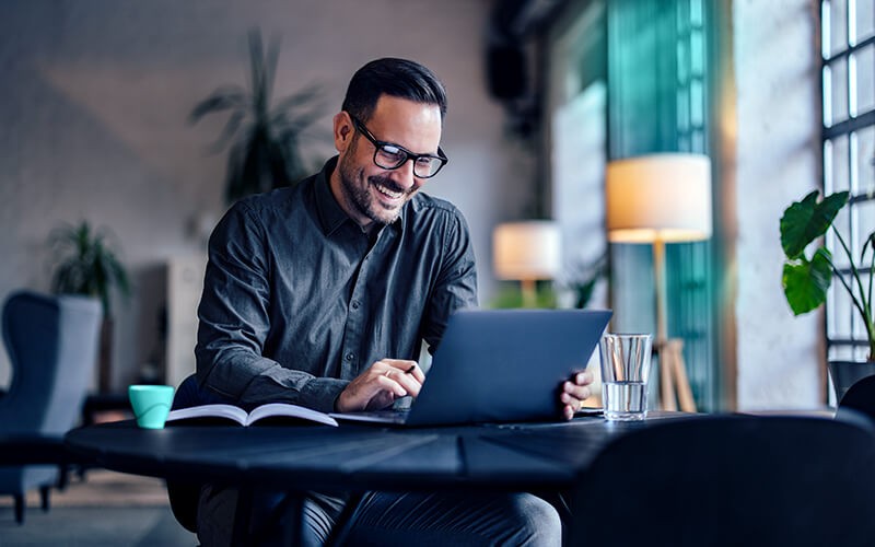 Man smiling using his laptop at the cafe