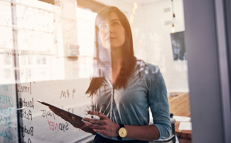 Woman holding tablet while thinking at white board