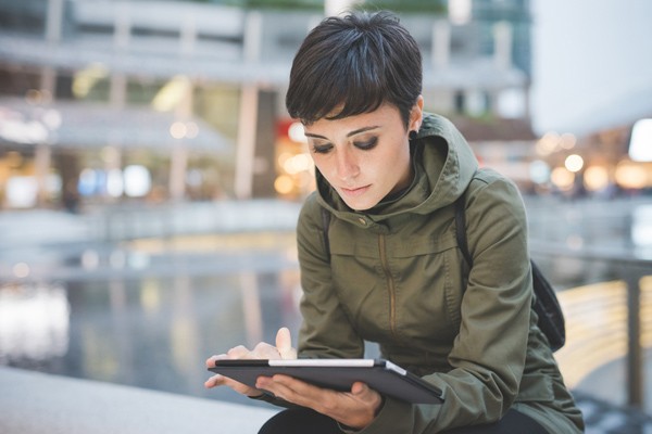 Woman looking at tablet Woman in coat sitting outside looking at tablet
