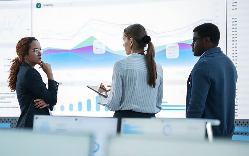 Group of business professionals gathered around screen displaying data analytics