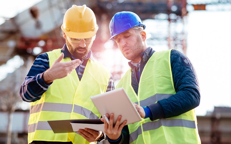 Two engineers at construction site looking at plans with tablet device